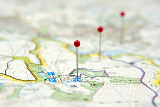 A close-up, shallow-focus shot of a paper map with three red pushpins marking different locations.