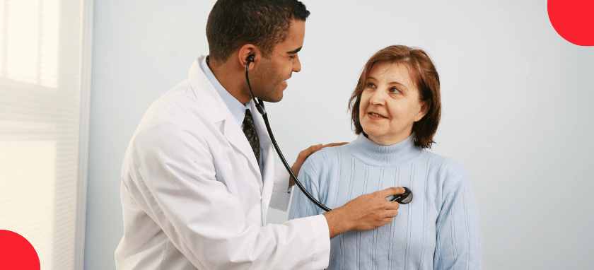 A doctor in a white coat using a stethoscope to perform a physical exam on a patient.