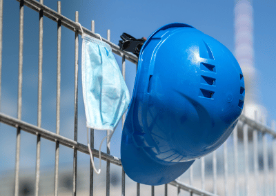 A blue hard hat and a surgical mask hanging on a wire fence.