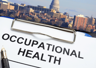 A clipboard with "OCCUPATIONAL HEALTH" text and a fountain pen over a cityscape of Madison, Wisconsin.