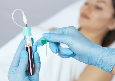 Gloved hands holding a test tube with a blood sample and a medical needle setup.