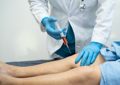 A healthcare professional in blue gloves administering a knee injection to a patient in blue scrubs.