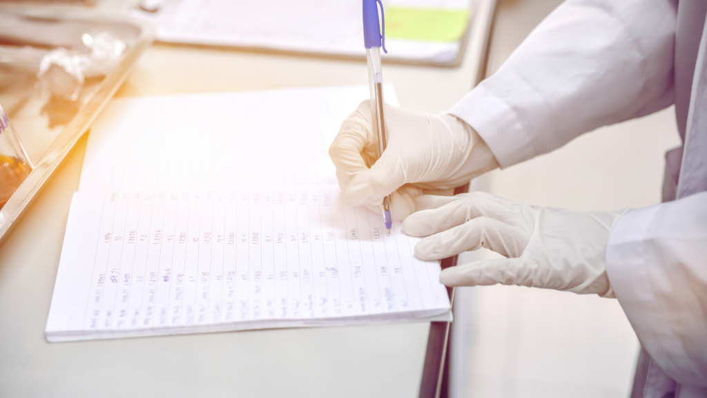 A person wearing a lab coat and latex gloves writes data on a paper form.