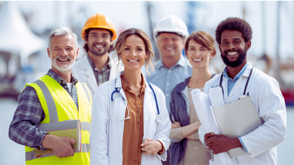 A diverse group of smiling professionals, including doctors in white coats and engineers in hard hats and safety vests, standing together outdoors.