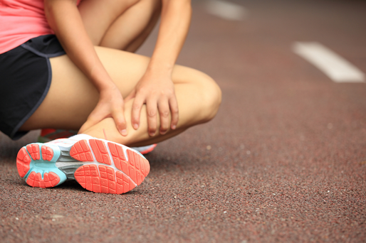A runner sitting on a paved track, clutching their calf muscle with both hands.