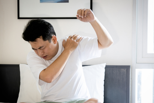 A man grimacing in pain while clutching his left shoulder.