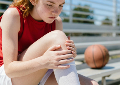 Close-up of a teenage basketball athlete holding her knee with mild pain while sitting on outdoor bleachers.