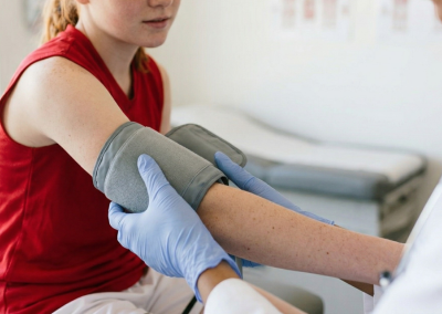 Healthcare provider placing a blood pressure cuff on a teenage athlete’s arm during a sports physical exam.