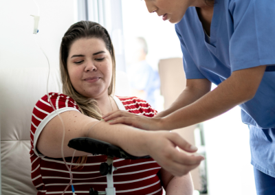 Nurse assisting an adult patient receiving IV hydration therapy in a medical clinic setting.