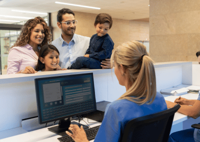 A family with two children checks in with a healthcare staff member at a medical reception desk.